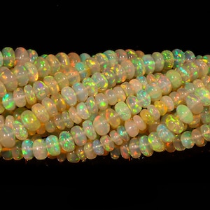 May include: Strands of opal beads with a mix of colors, including white, yellow, and hints of green and orange. The beads are oval-shaped and have a polished, iridescent surface. The background is black.