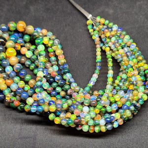 Puede incluir: Una colecci&oacute;n de cuentas de &oacute;palo redondas y multicolores ensartadas en un hilo fino. Las cuentas muestran un espectro de tonos iridiscentes que incluyen verde, azul, amarillo y naranja, con una calidad transl&uacute;cida que capta la luz.