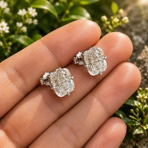 Puede incluir: Un par de pendientes de botón con piedras rectangulares de talla cojín y una superficie facetada y brillante. Cada piedra está engastada en una montura de metal plateado con garras, mostrando un aspecto claro y resplandeciente.