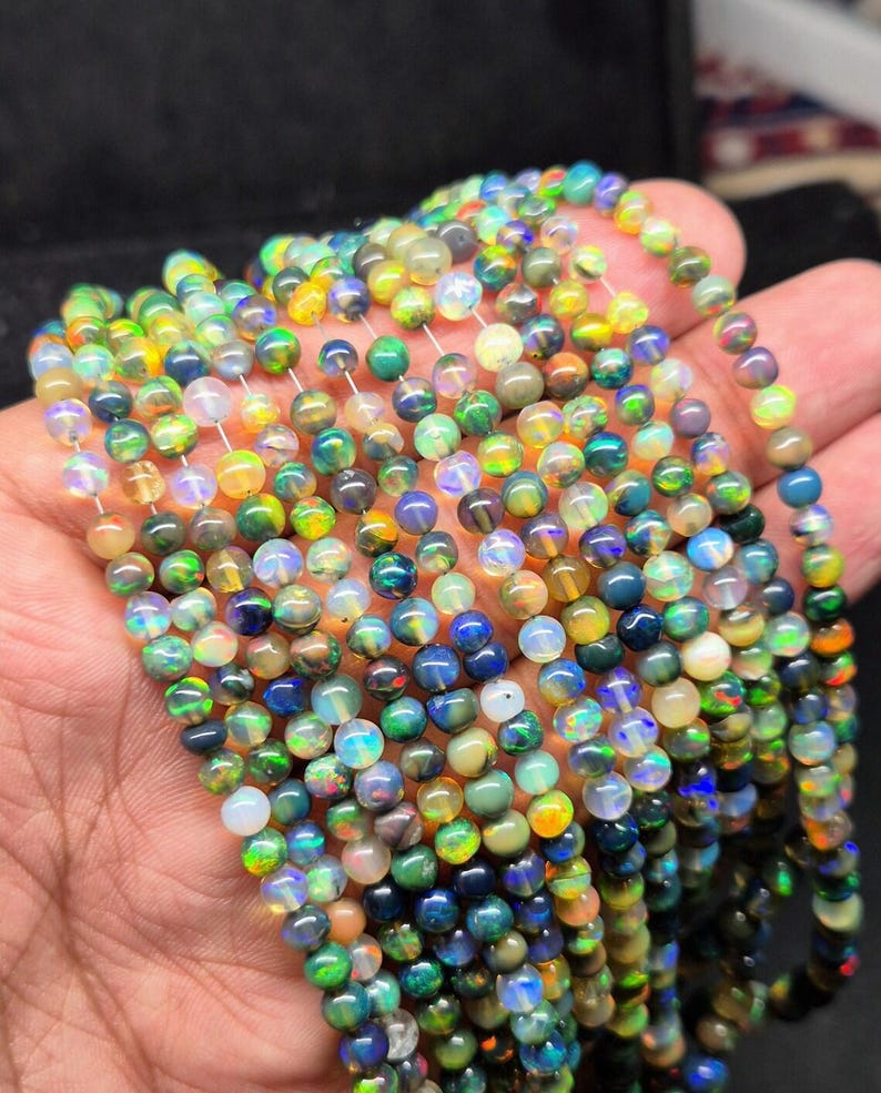 May include: Strands of colorful opal beads. The beads display a variety of colors, including blues, greens, yellows, and oranges. The beads are round and appear to be strung together, creating a necklace or bracelet.