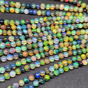 Puede incluir: Una colecci&oacute;n de cuentas de &oacute;palo redondas y multicolores dispuestas en varios hilos paralelos. Las cuentas exhiben una calidad transl&uacute;cida con destellos vibrantes de luz verde, azul, naranja y amarilla que se reflejan desde cada esfera individual.