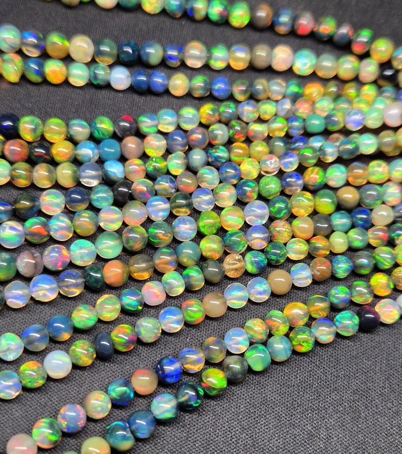 Puede incluir: Una colecci&oacute;n de cuentas de &oacute;palo redondas y multicolores dispuestas en varios hilos paralelos. Las cuentas exhiben una calidad transl&uacute;cida con destellos vibrantes de luz verde, azul, naranja y amarilla que se reflejan desde cada esfera individual.