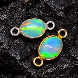 Può includere: Due connettori per gioielli di forma ovale con opali iridescenti. Un connettore è incastonato in una montatura in metallo color argento, l'altro in una montatura in metallo color oro. Ogni pezzo ha due piccoli anelli circolari alle estremità.