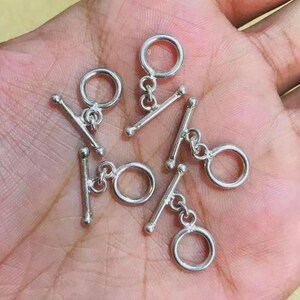 May include: Close-up of several silver toggle clasps. Each clasp has a T-bar and a ring, connected by a small chain. These clasps are likely for jewellery making or crafts, providing a secure closure for necklaces or bracelets.