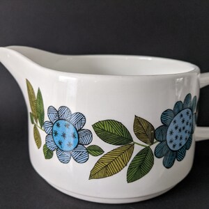 Puede incluir: Salsera de cerámica blanca con un diseño floral azul y verde. El diseño presenta flores y hojas estilizadas.
