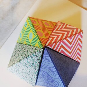 May include: A geometric paper sculpture made of five triangular panels. Each panel features a different colorful pattern: yellow and green, red and white, green and white, blue and white, and red and orange.