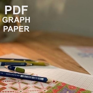 May include: A close-up of a sheet of graph paper with a colourful design drawn on it. The design features red, green, purple, and orange colours. A blue pencil is lying on the paper.