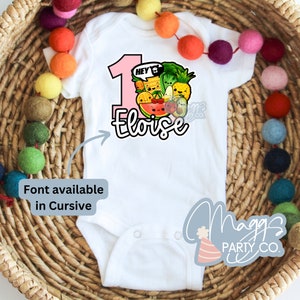 Op de afbeelding: Een witte baby romper met een roze nummer &eacute;&eacute;n en de tekst "Hey I'm Eloise" in een cursief schrift. Het nummer &eacute;&eacute;n is omringd door een kleurrijke illustratie van fruit en groenten. De romper heeft een witte achtergrond en is versierd met een kleurrijk fruit- en groenteontwerp. De romper is gemaakt van een zacht, comfortabel materiaal en is perfect voor de eerste verjaardag van een baby.