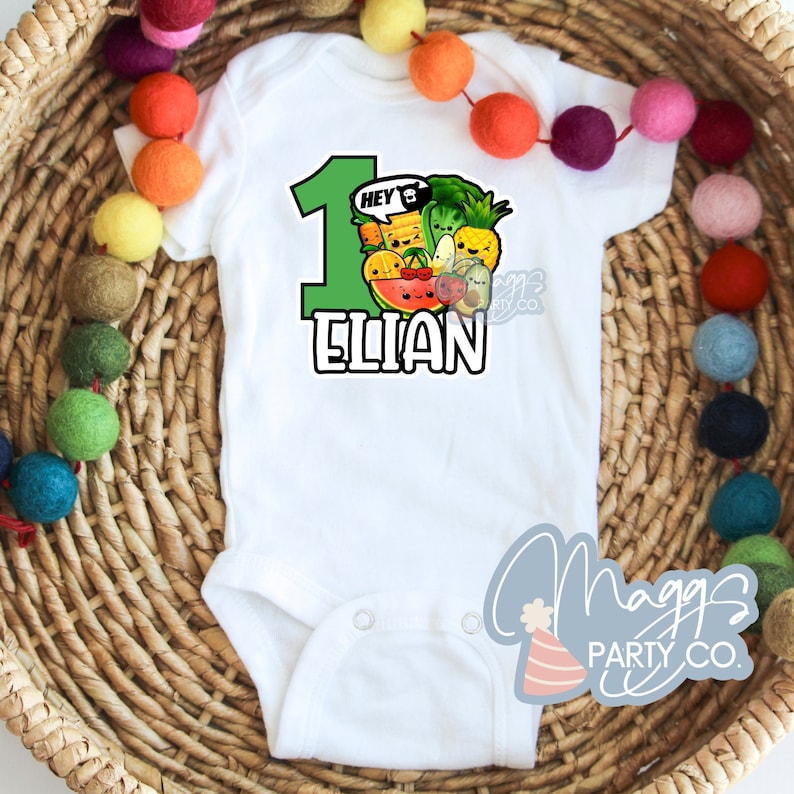 Op de afbeelding: Witte romper met een groen nummer &eacute;&eacute;n en de naam "Elian" in zwart. Het nummer &eacute;&eacute;n is versierd met cartoon fruit en groenten. De tekst "Hey!" staat in een spraakballon boven het nummer &eacute;&eacute;n.