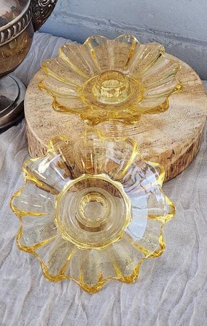 May include: Two matching amber-colored glass candle holders featuring a scalloped, flower-like petal design. Each piece has a central circular depression for a candle, with translucent yellow glass radiating outward in a textured, fluted pattern.