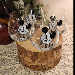 Puede incluir: Juego de cuatro copas de vino sin tallo transparentes. Cada copa presenta un dise&ntilde;o de personaje de dibujos animados en blanco y negro. Las copas se exhiben sobre una base de madera r&uacute;stica. Perfecto para una fiesta tem&aacute;tica o uso diario.