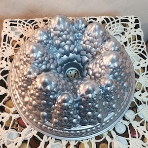 Puede incluir: Un molde para bizcocho de color plateado con un diseño texturizado único. El molde tiene un tubo central y una serie de formas redondeadas en forma de burbujas. Este molde para hornear es perfecto para crear pasteles decorativos.