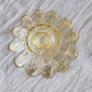 May include: A clear glass bowl with a golden yellow tint, featuring a scalloped edge and a textured, crackled finish throughout the surface. The bowl has a circular base and a wide, petal-like rim that radiates outward from the center.