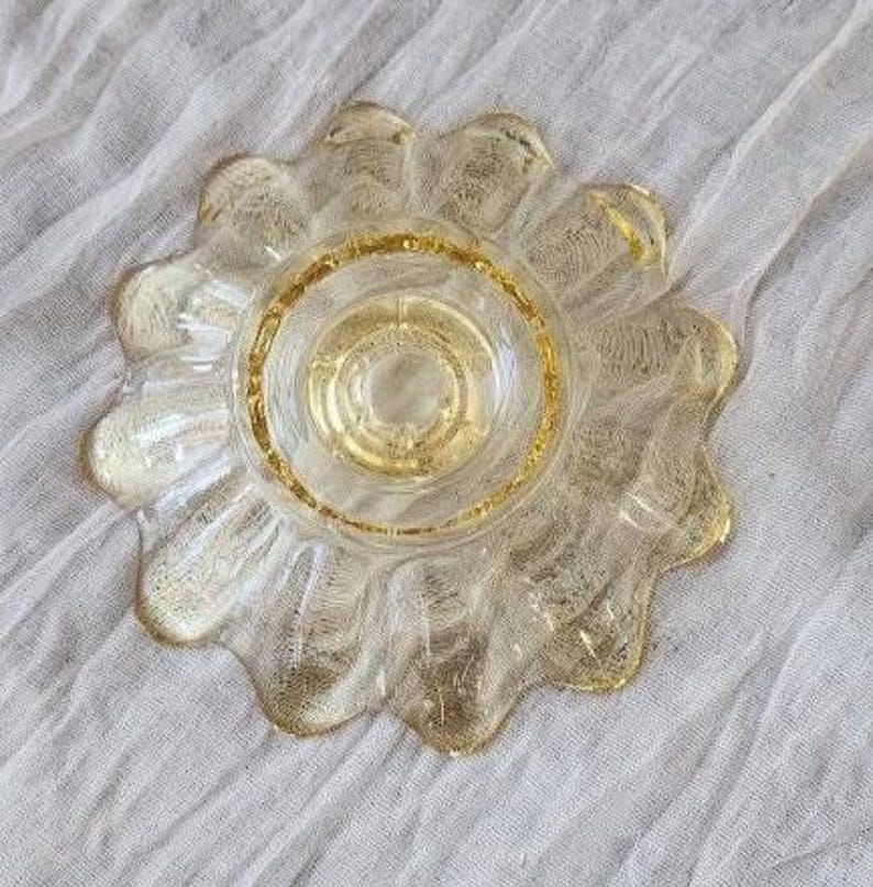 May include: A clear glass bowl with a golden yellow tint, featuring a scalloped edge and a textured, crackled finish throughout the surface. The bowl has a circular base and a wide, petal-like rim that radiates outward from the center.