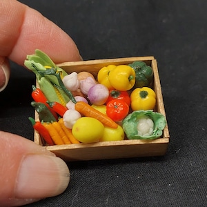 Puede incluir: Una caja de madera llena de verduras en miniatura, incluyendo zanahorias, pimientos, maíz, ajo, cebollas y una col. Las verduras están hechas de arcilla y están pintadas en colores realistas.
