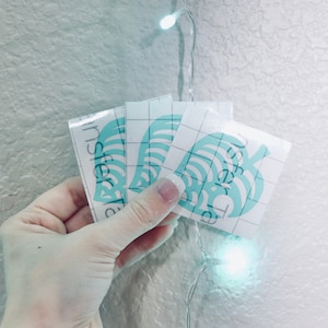 May include: Three white vinyl stickers with a light blue leaf design. The stickers have a grid pattern on the back and the text "Transfer Tape" printed on the side.
