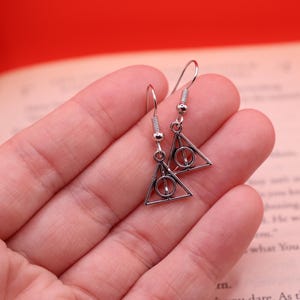 May include: Silver earrings with a triangle pendant featuring the Deathly Hallows symbol from the Harry Potter series.