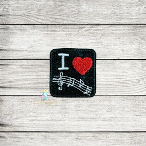 May include: Black square patch with the text "I", a red heart, and musical notes. The patch has a white border and is on a light wood grain background.