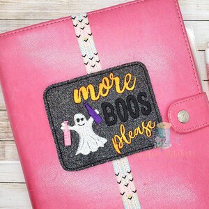 May include: A black and grey glitter patch with a white ghost holding two purple bottles and the text "more boos please" in orange.