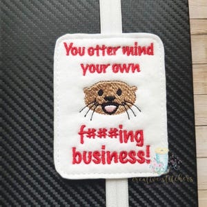 May include: White bookmark with red embroidery that says "You otter mind your own f***ing business!" with a cartoon otter face in the middle.