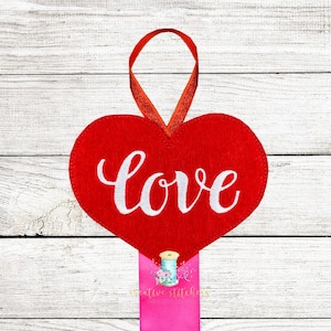 Peut inclure: Ornement en forme de cœur rouge en feutre avec le mot "love" en écriture blanche. Il est suspendu à un ruban rouge et un ruban rose avec un logo. Parfait pour la Saint-Valentin ou une occasion similaire.