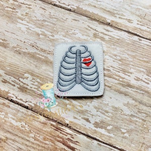 May include: A white felt patch with an embroidered image of a ribcage with a red heart in the center. The patch is perfect for adding a unique touch to clothing, bags, or other crafts.