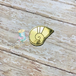 May include: A gold-colored seashell with a textured surface. The seashell is a popular motif in nautical and ocean-themed crafts.