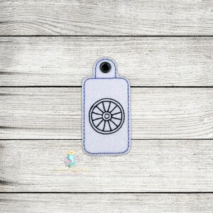 May include: White key chain with a blue border and a black and white wheel design in the center.