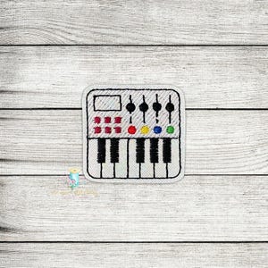 Puede incluir: Parche blanco bordado de un sintetizador con teclas negras, botones rojos, amarillos, azules y verdes, y una pantalla blanca.