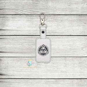 May include: White leather keychain with a silver key ring and an embroidered all-seeing eye design.
