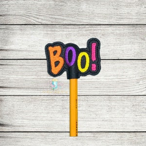 Könnte beinhalten: Ein schwarzer Bleistifthalter mit dem Wort "BOO!" in orange, lila und gelben Buchstaben. Der Halter ist auf einem gelben Bleistift.