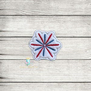 May include: A white felt applique with a red and blue starburst design. The starburst has a white centre and red and blue rays radiating outwards.