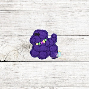 May include: Purple felt applique of a dog wearing a Mardi Gras beaded necklace. The dog is in a sitting position with its head tilted to the side.