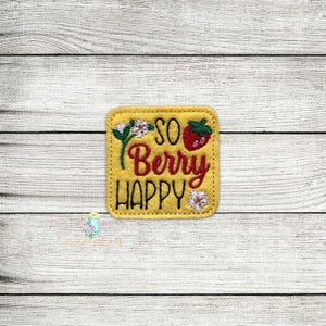 May include: A yellow felt patch with embroidered text that reads "So Berry Happy". The text is in black with a red strawberry and white flowers.