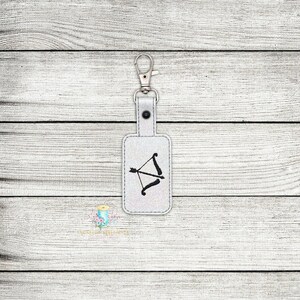 May include: White leather keychain with a silver key ring and a black embroidered bow and arrow design.