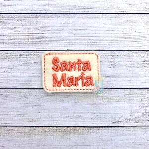 May include: A white felt patch with a red embroidered border and the text "Santa Maria" in red.
