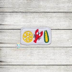 Puede incluir: Parche blanco bordado con un limón, una langosta roja y una mazorca de maíz verde y amarilla.