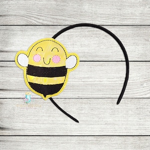 Può includere: Un cerchietto a forma di ape giallo e nero con un viso sorridente e guance rosa. Il cerchietto è fatto di feltro nero ed è perfetto per un costume da bambino o una festa.