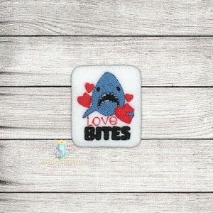 May include: White felt patch with an embroidered blue shark with red hearts and the text "Love Bites".