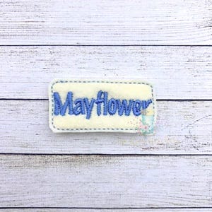 May include: A white felt patch with blue embroidered lettering that reads "Mayflower".