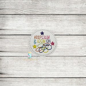 Może przedstawiać: Biała, okrągła, haftowana naszywka z napisem "Keep Calm & Loom On" w kolorowej nici. Naszywka przedstawia gwiazdę i serię kolorowych pierścieni, z gwiazdą po każdej stronie. Naszywka znajduje się na jasnej powierzchni z usłojeniem drewna.