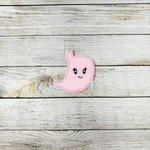 May include: Pink felt stomach with a cartoon face. The stomach has black eyes, a black mouth, and a pink outline.