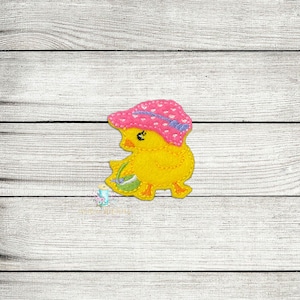 May include: A yellow chick wearing a pink and white polka dot hat with a purple bow. The chick is holding a green and white egg in its wing.