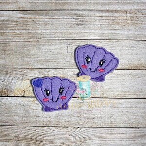 May include: Two purple felt appliques of seashells with smiling faces. The seashells have a 3D effect.