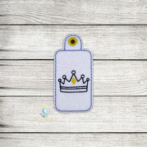 May include: A white fabric key tag with a blue outline and a black and yellow crown design.