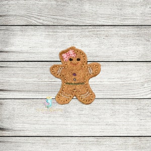 May include: A gingerbread person applique with a pink and white bow on its head. The gingerbread person is brown with yellow icing details and is smiling.