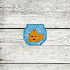 May include: A blue felt fishbowl with a smiling orange goldfish inside. The fishbowl has white felt bubbles around the goldfish.