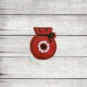 May include: Red felt bag with a black string tie and a white eye with a black pupil. The bag is a Christmas ornament.
