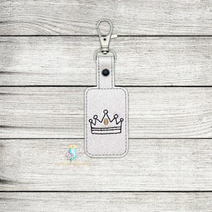 May include: White leather keychain with a silver key ring and a black embroidered crown.