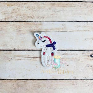 May include: White felt unicorn applique with a purple and pink scarf. The unicorn has a rainbow horn and closed eyes.